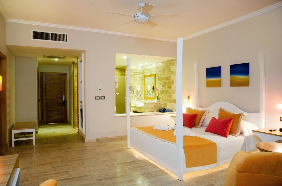 Evening Junior Suite with orange and red pillows, an open view into the stone jacuzzi bathroom and the entry door